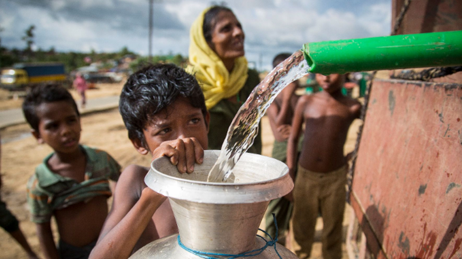 Niño refugiado rohingya y otros esperando el agua que se reparte en un contenedor