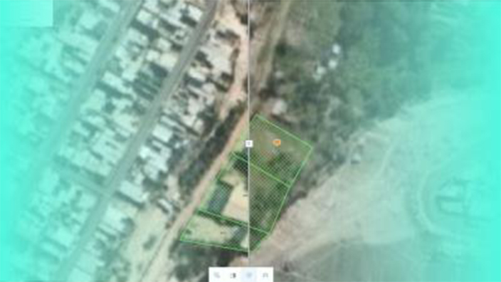 Una foto aérea de un pueblo de pequeñas cabañas marrones en una llanura verde con montañas distantes silueteadas contra una puesta de sol naranja pálido