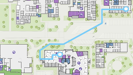 Mapa digital con edificios cuadrados, árboles verdes y una ruta resaltada en azul que muestra la orientación en un gran campus