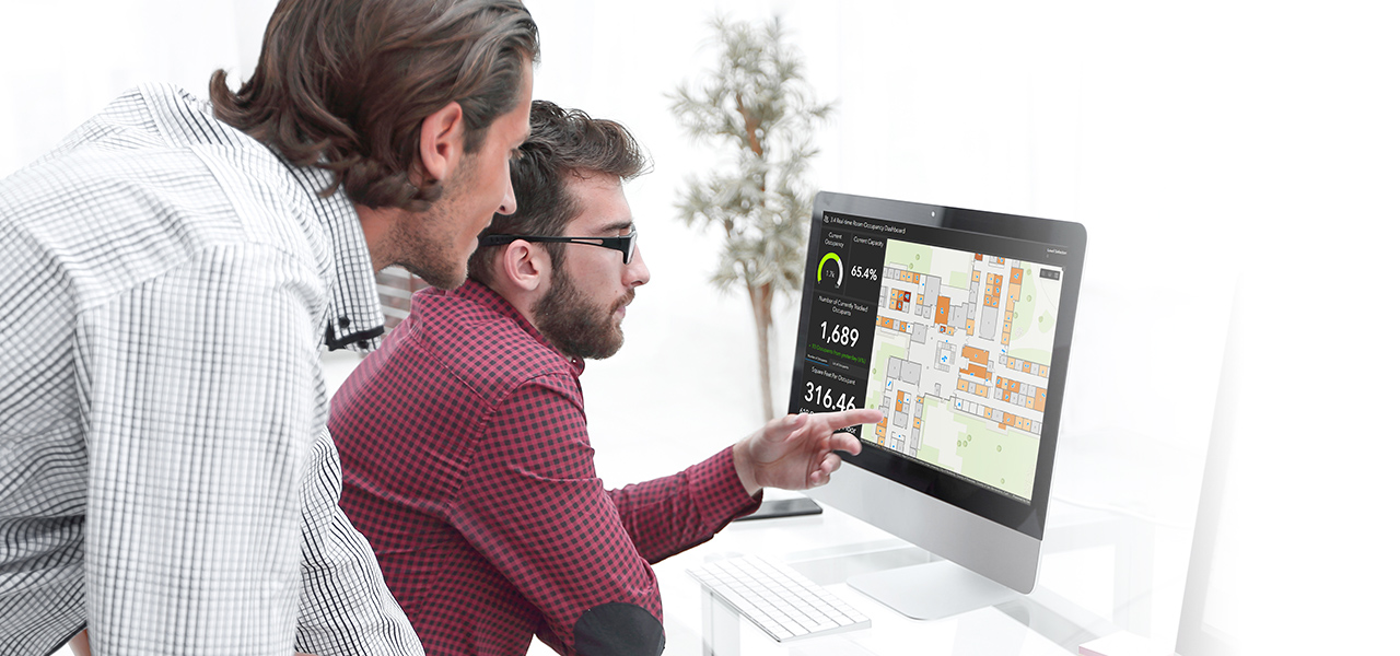Dos hombres mirando una pantalla de ordenador que muestra un mapa azul y rosa que representa los datos del SIG para la planificación del espacio interior
