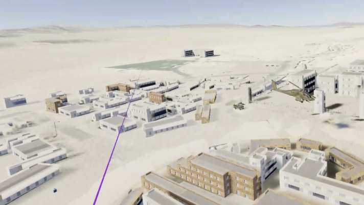 Representación virtual de una base en el desierto con edificios beis y grises en 3D, un helicóptero y una línea morada 